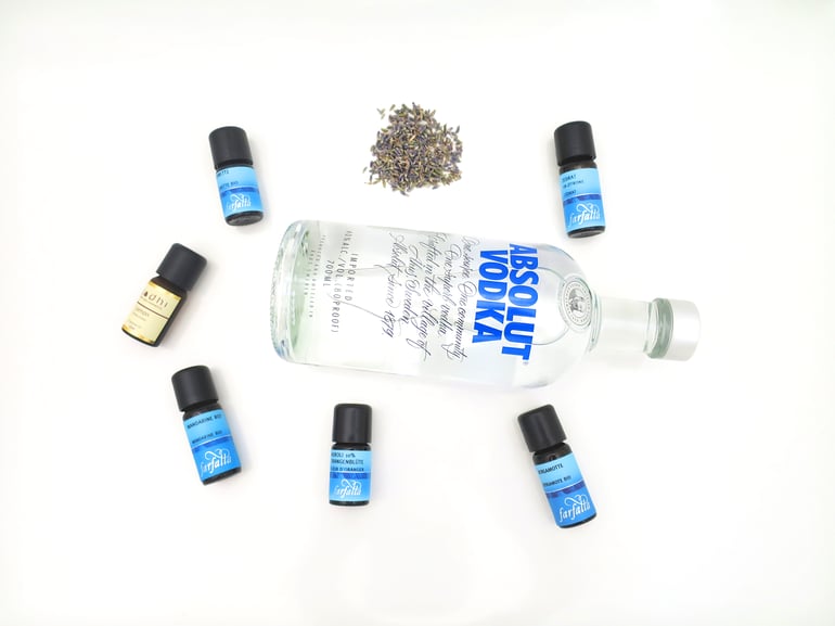 Eine Wodka Flasche liegt auf weisem Grund umgeben von kleinen ätherischen Öl Fläschchen