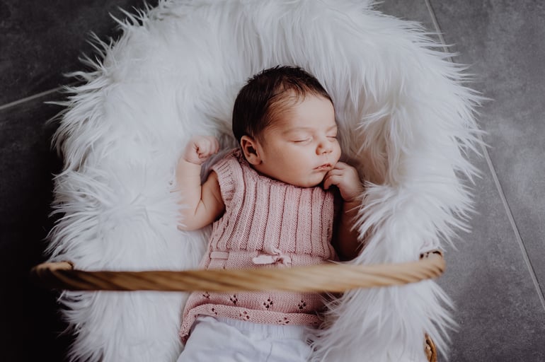 Neugeborenes Babymädchen liegt im Weidenkorb auf weißem Fell fotografiert von Uschi Kitschke aus Kreuzau.