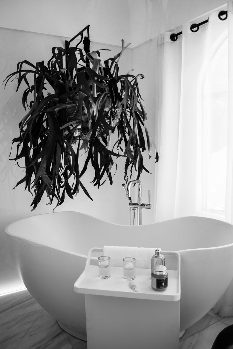 A luxurious bathroom features a large white freestanding bathtub, complemented by floor-mounted chrome sleek shower rail, timber-look floor tiles, with a chic bathroom trolley stocked with soaps and accessories evoking the element