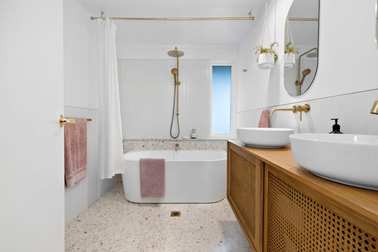 a modern design with a freestanding bathtub, gold fixtures, a light terrazzo floor, and a wooden vanity with double sinks, creating a stylish and clean space.