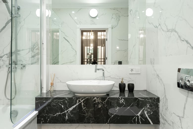 This elegant bathroom showcases luxurious marble walls and countertops, with a vessel sink, a glass-enclosed shower, and sleek black and white accents for a sophisticated, modern look