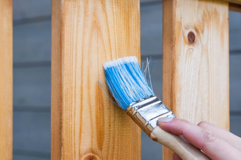 homeowner applying a clear wood finish or varnish to a wooden surface with a paintbrush.