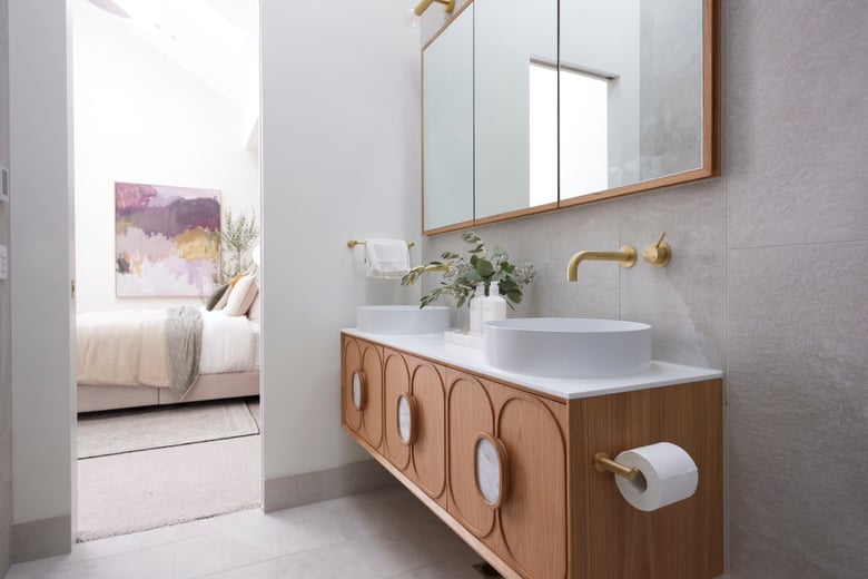 a contemporary bathroom with a stylish wooden vanity, circular cabinet details, gold fixtures, and a minimalist aesthetic that seamlessly connects to a cozy bedroom beyond.