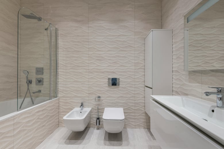 This modern bathroom features a sleek design with textured wave-patterned wall tiles, a glass-enclosed shower, a bidet, and a wall-mounted toilet, creating a clean and minimalist aesthetic