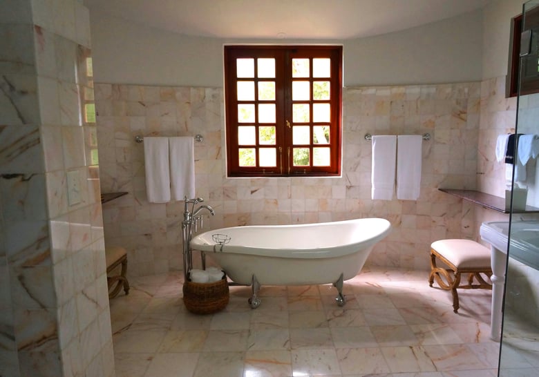 A serene and elegant bathroom with a freestanding clawfoot bathtub, set against warm, natural light streaming through a wooden window, surrounded by marble tiles.