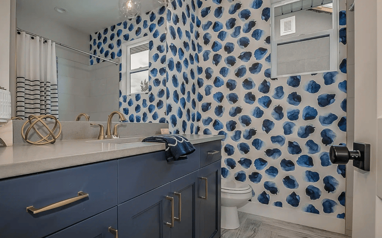 The bathroom showcases a dark blue vanity with brushed gold finish mixers, a classic white toilet, a striking blue and white feature wall, and a cozy shower area with a stylish curtain.