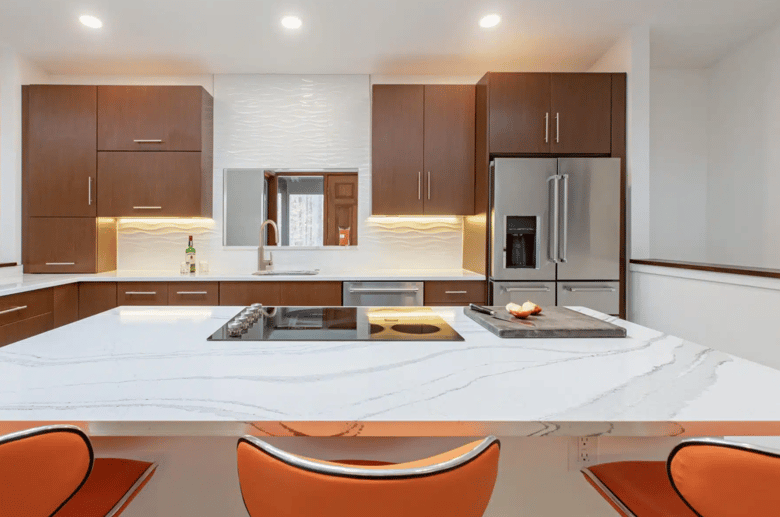 This is a modern kitchen with sleek wooden cabinetry, a white marble-like countertop, integrated appliances, and warm under-cabinet lighting, giving it a clean yet inviting look.