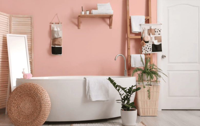 The bathroom features a spacious white freestanding bathtub with chrome mixers, oak timber floor tiles, lush potted plants, a large floor-standing mirror, and a rustic timber ladder holding towels.