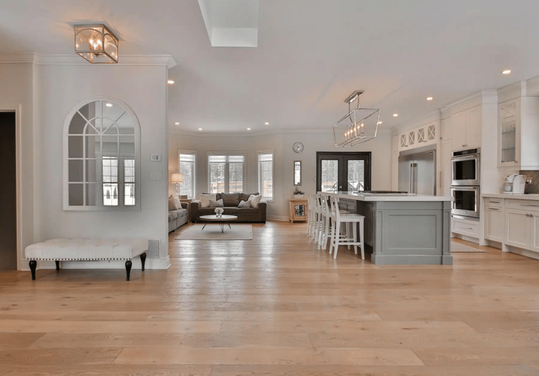 Large kitchen with a 40mm white stone benchtop, a grey island with large pendant lights, white cabinets with glass display doors, light oak floating floorboards, dual stainless ovens with a steamer, and a spacious French door fridge.