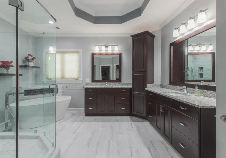 a spacious, modern bathroom with dark wood cabinetry, granite countertops, a glass-enclosed shower, and a freestanding bathtub, all set against light gray walls and flooring.