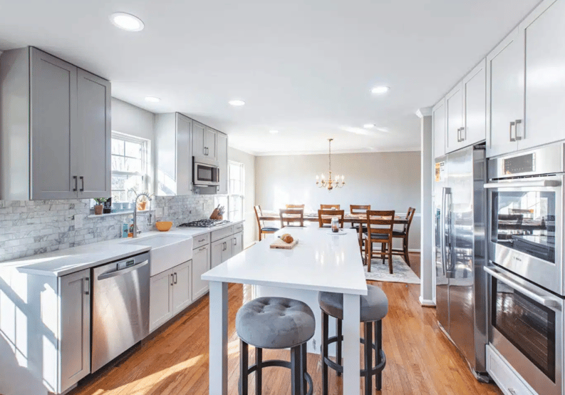a bright and spacious kitchen with gray cabinetry, a large central island with seating, stainless steel appliances, and an adjacent dining area illuminated by natural light.