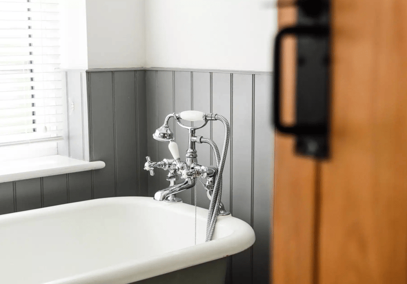 a vintage-style bathtub with a classic chrome faucet set, complemented by grey wainscoting and a softly lit window.