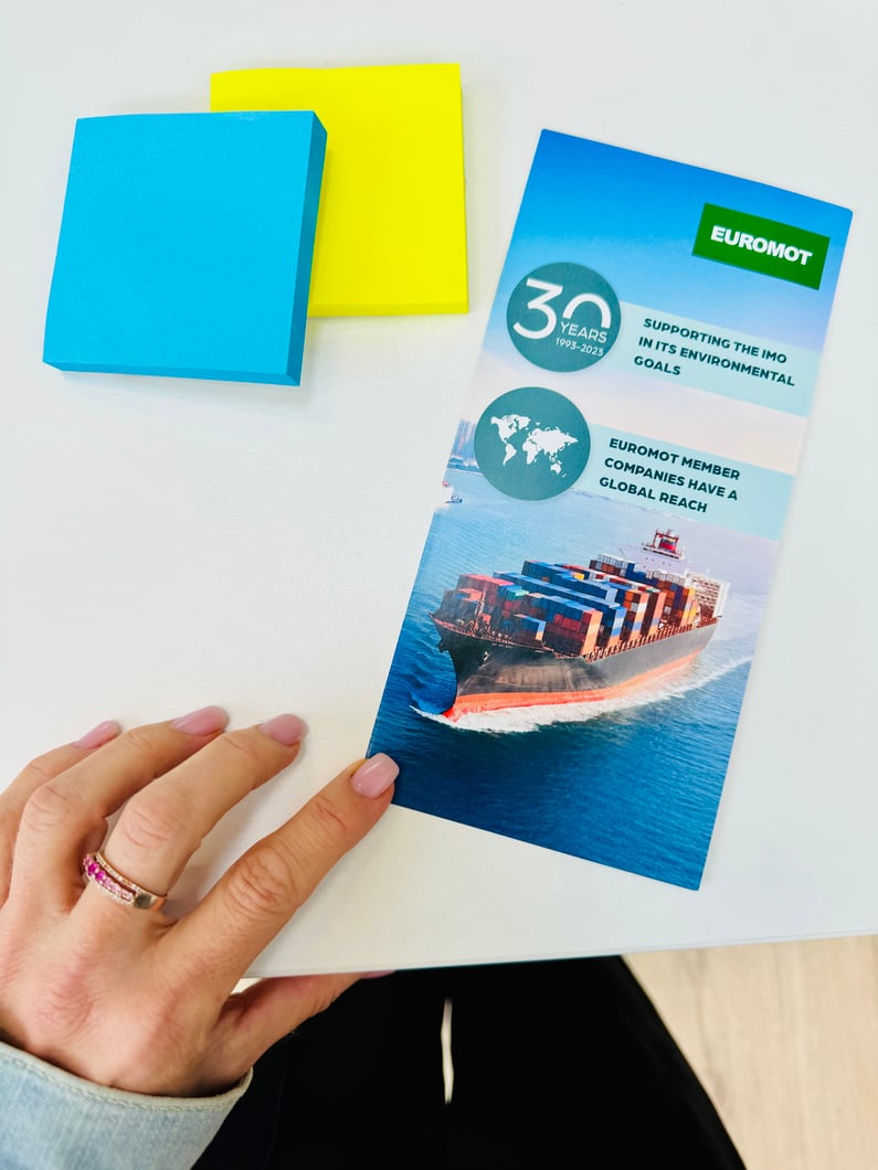 Hand hält ein EUROMOT-Flyer mit Containerschiff, daneben farbige Haftnotizen – visuelles Beispiel für Printdesign und Kommunikationsmaterial.