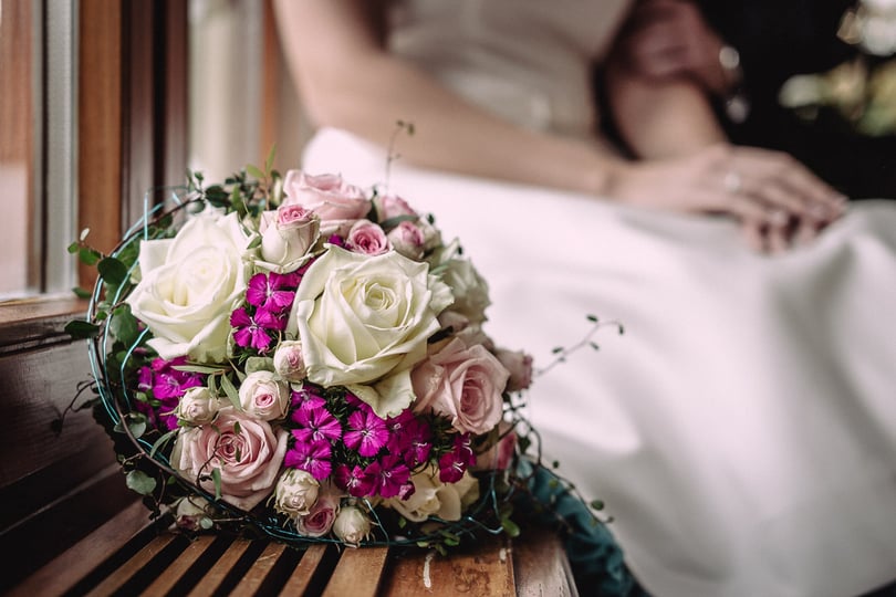 Ein farbenfroher Brautstrauß vor einem sich umarmenden Hochzeitspaar