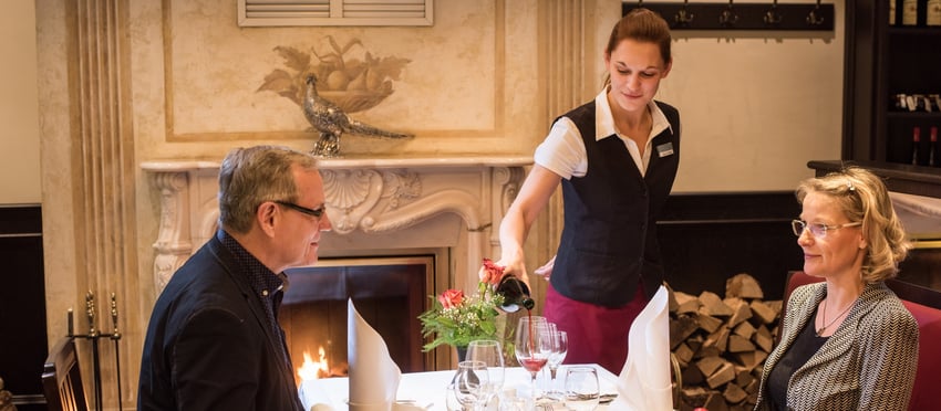 Frau und Mann bei einem Dinner mit Bedienung die Wein einschänkt