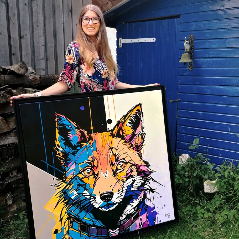 Die Künstlerin Maria Kley steht hinter einem abstrakten Acrylgemälde. Die Auftragskunst im Schattenfugenrahmen zeigt einen Fuchskopf.