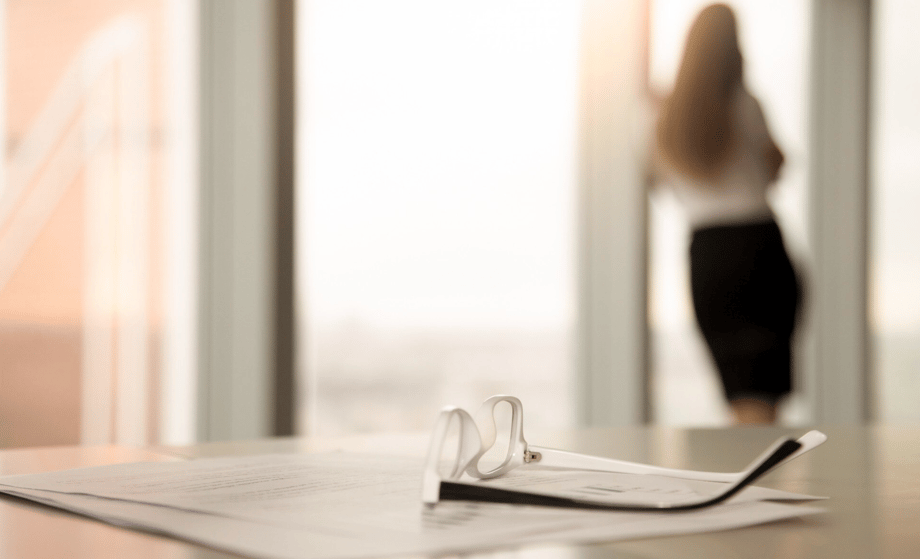 Arbeitsvertrag mit Brille im Vordergrund, unscharfe Frau am Fenster im Hintergrund – Symbolbild für verhaltensbedingte Kündigung und Datenschutz