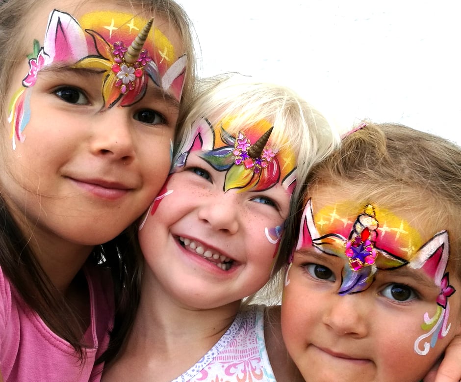 Drei Mädchen sind in Regenbogenfarben als Einhörner geschminkt.