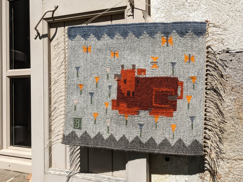 Un kilim-tenture murale en tissage représentant un veau de vache salers qui se repose sur un pré de crocus. Dessin du tissage mural géométrisé.