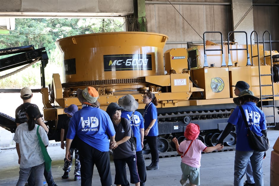 廃木材チップ化の機械の前で説明しています