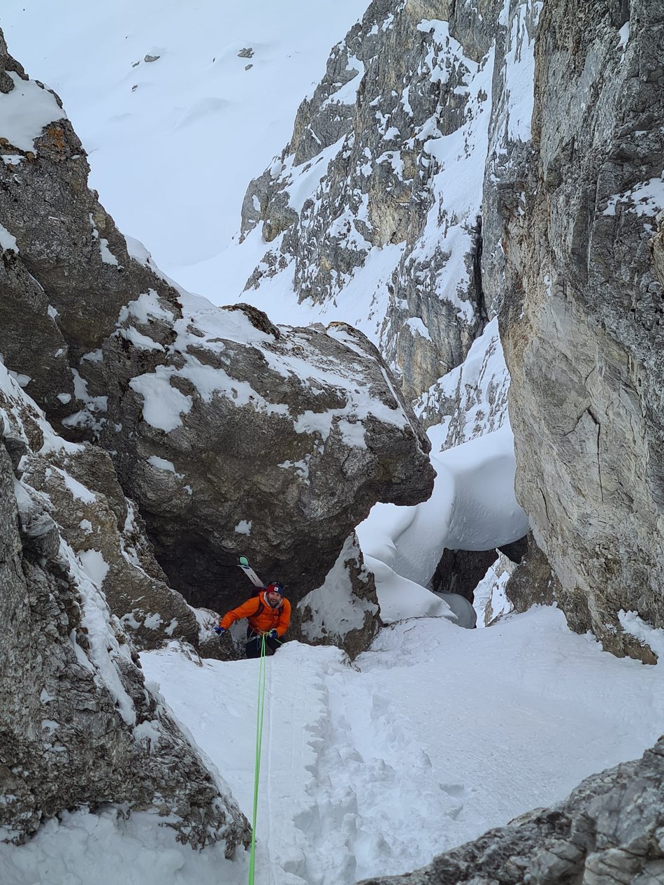 Bergführer steigt am Seil durch einen Felsdurchgang auf um danach eine Freeride Abfahrt zu geniessen