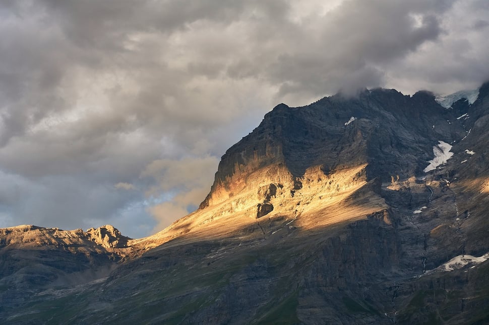 The image shows the photograph of mountain that is illuminated by evening sunlight against a clouded sky.