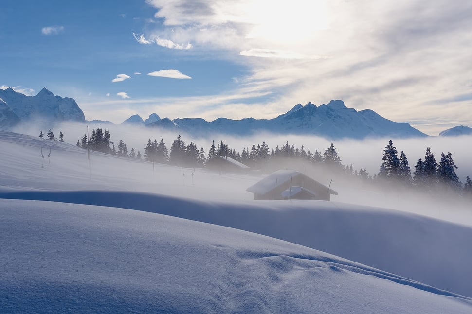 The image shows the photograph of an alpine pasture with a mountain hut in winter. A mountain range is visible in the background. The location is Balisalp (Hasliberg).