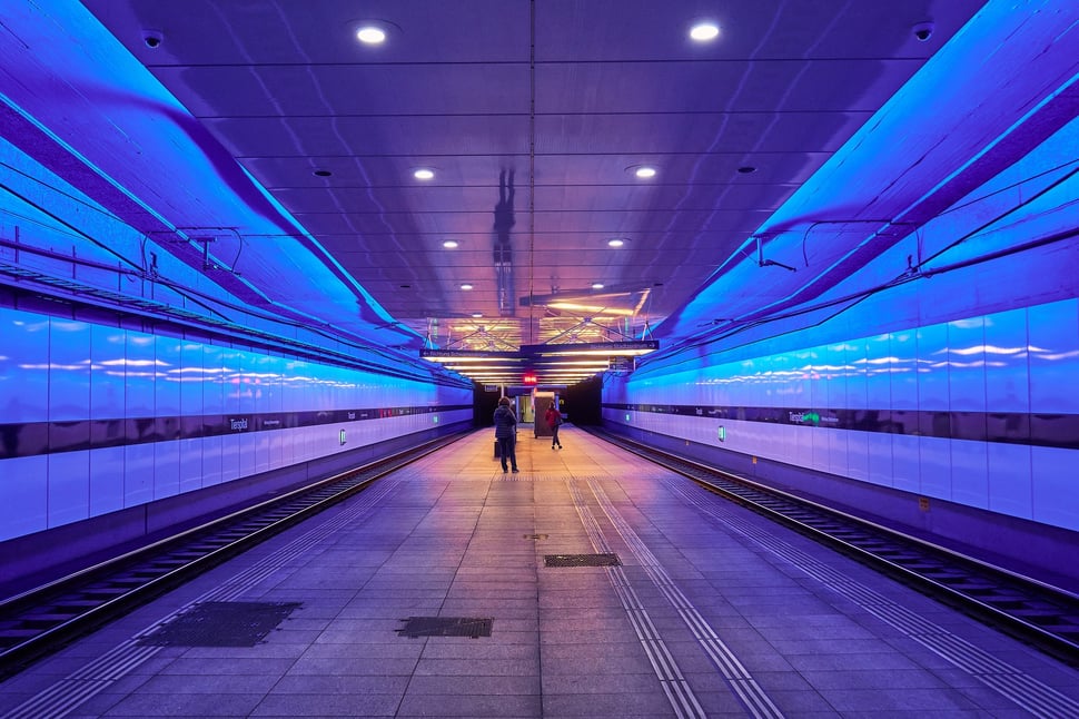 The image shows the photograph of two waiting people in a subway tram station in Zurich from a symmetrical perspective.   