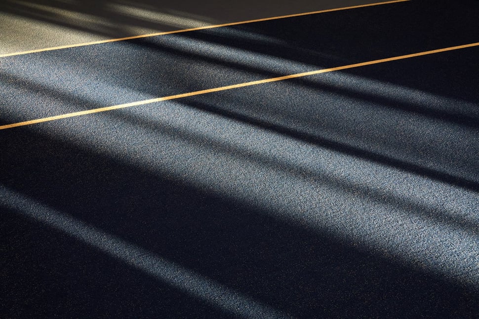 The image shows the photograph of a tennis court, which is flooded by sunlight.