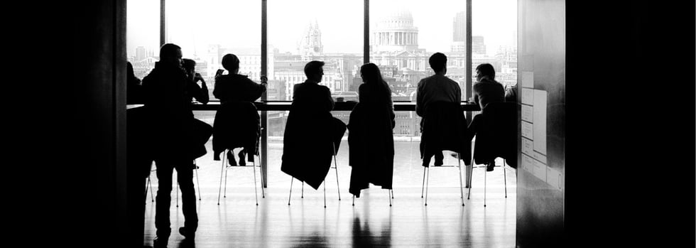 Menschen sitzen an einem Tresen mit Aussicht auf die Stadt und unterhalten sich in kleinen Gruppen.